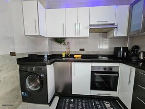 A compact kitchen with a washing machine, oven, and a sink. - Charming 2-bedroom Apartment in Martil, Morocco (Martil)