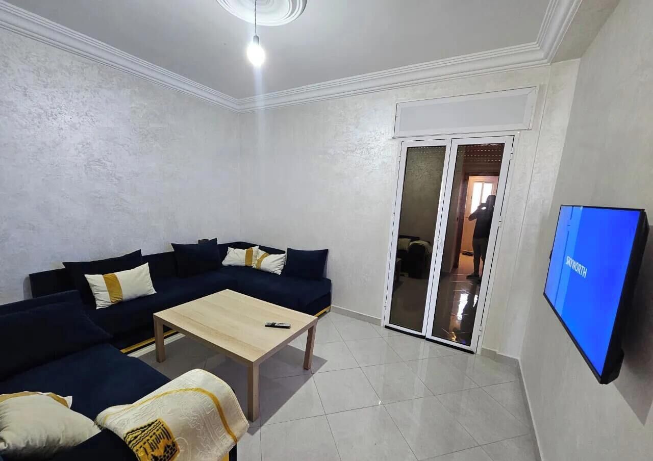 A living room with a dark blue sofa set, a wooden coffee table, and a flat-screen TV mounted on the wall.