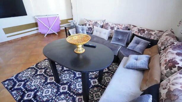 A living room with a round black table, a sofa with floral upholstery, and a patterned rug. - Charming 1-bedroom Apartment With Piscine in Martil (Martil)