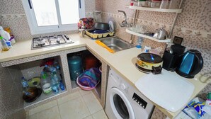 A compact kitchen with a gas stove, sink, and a washing machine. - Charming 1-bedroom Apartment With City View in Martil (Martil)