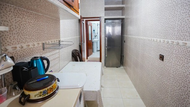 A narrow kitchen with a refrigerator, a kettle, and a coffee maker on the counter. - Charming 1-bedroom Apartment With City View in Martil (Martil)