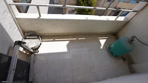 Uma varanda com guarda-corpo de metal, um cano de água e um cilindro de gás verde.