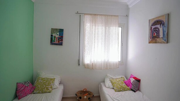 A room with two beds, a window with sheer curtains, and two paintings on the walls. - Charming 2-bedroom Apartment in Martil, Morocco (Martil)