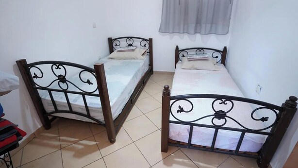 A room with two single beds with metal frames and wooden headboards, a window with a sheer curtain, and a tiled floor. - Charming 2-bedroom Apartment in Martil,morocco (Martil)