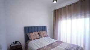 A bedroom with a bed, a nightstand, and a window with curtains. - Charming 2-bedroom Apartment in Martil,morocco (Martil)