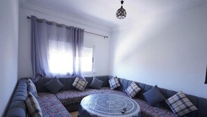 A modern living room with a sectional sofa, patterned rug, and a round coffee table. - Charming 2-bedroom Apartment in Martil,morocco (Martil)