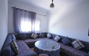 A modern living room with a sectional sofa, patterned rug, and a round coffee table. - Charming 2-bedroom Apartment in Martil,morocco (Martil)