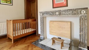 Une pièce avec un berceau en bois, une cheminée ornée de marbre et un tableau encadré accroché au mur.