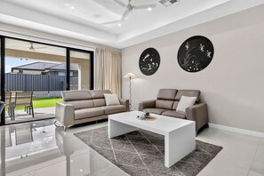 A modern living room with two sofas, a coffee table, and a large window. - Leeds House | 4BR New Build, Alfresco, 15 Min CBD (Northfield)
