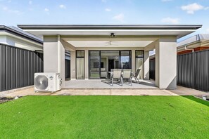Ein modernes Haus mit überdachter Terrasse, Rasenfläche und einer großen Klimaanlage.