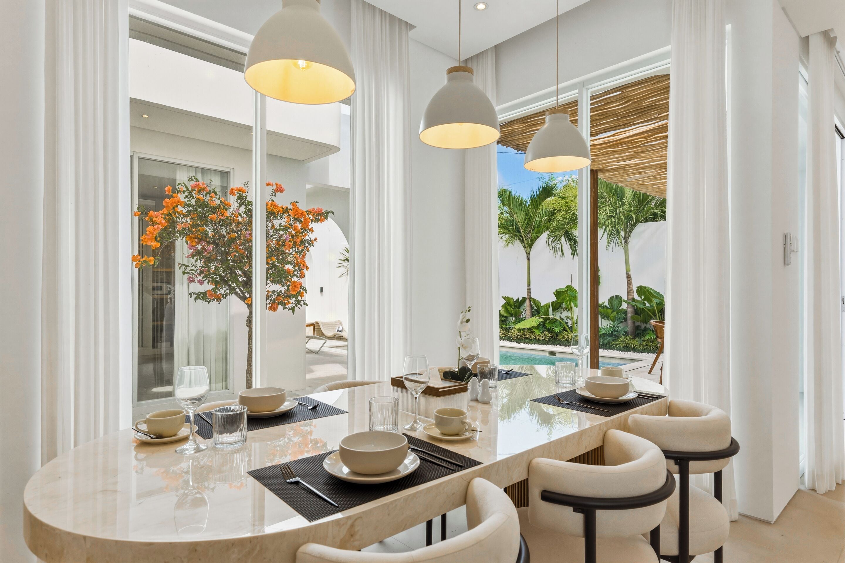 A modern dining area with a marble table, white chairs, and pendant lighting.
