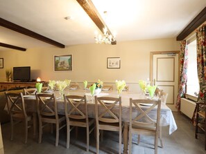 Ein Essbereich mit einem langen Tisch, der für eine Mahlzeit gedeckt ist, Holzstühlen, einer Chandelierleuchtre und gerahmten Bildern an der Wand.