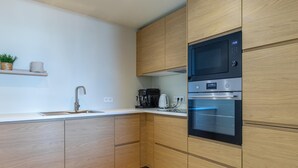Une cuisine moderne avec des meubles en bois, un évier en acier inoxydable et des appareils électroménagers intégrés, notamment un four à micro-ondes et un four traditionnel.