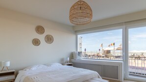 Une chambre avec un grand lit, une table de chevet avec une lampe, une fenêtre donnant sur la plage et un luminaire au plafond.