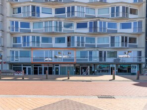 Ein mehrstöckiges Gebäude mit Balkonen, einem Eingangsbereich und einem sichtbaren Geschäft mit Beschilderung.