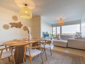 A modern living room with a dining area, featuring a large window, a sofa, and a dining table with chairs. - A beautifully renovated flat on the Zeedijk (Blankenberge)