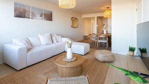 Un salon moderne avec un canapé blanc, une table basse ronde et un coin repas comprenant une table et des chaises en bois.