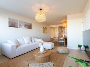 A modern living room with a white sofa, a round coffee table, and a dining area with a wooden table and chairs. - A beautifully renovated flat on the Zeedijk (Blankenberge)