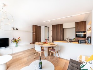 A modern kitchen with a dining area, a flat-screen TV, and a sofa.