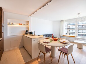 A modern kitchen with a dining area, a coffee machine, and a window with a view of buildings.