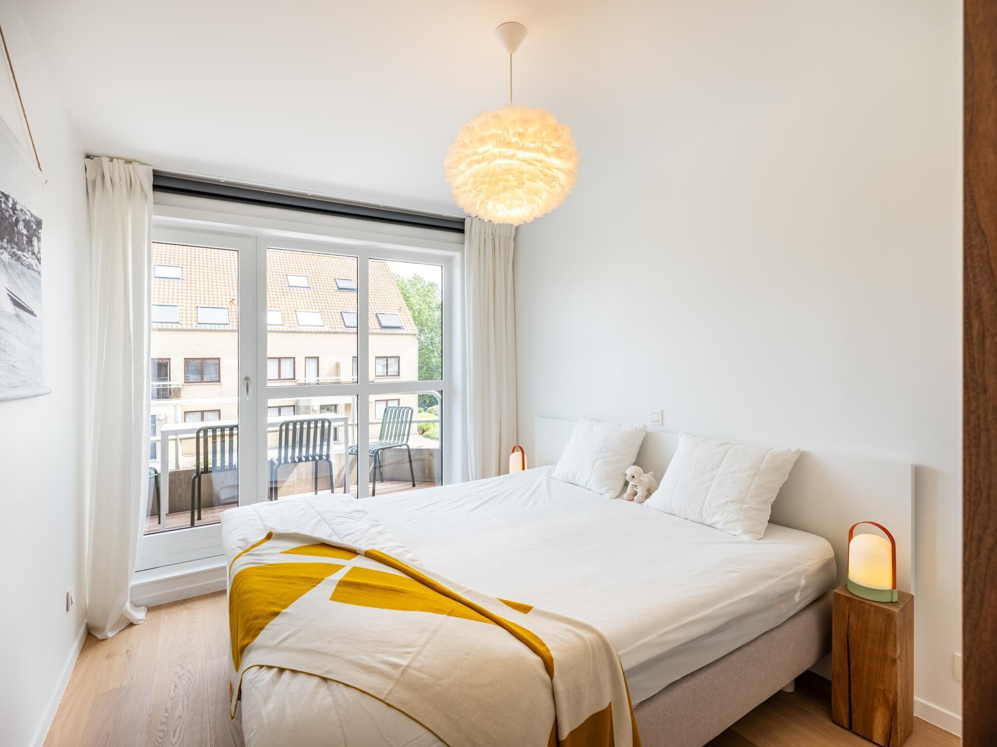 Quarto com uma cama grande, janela com cortinas, luminária pendente e mesa de cabeceira com abajur.