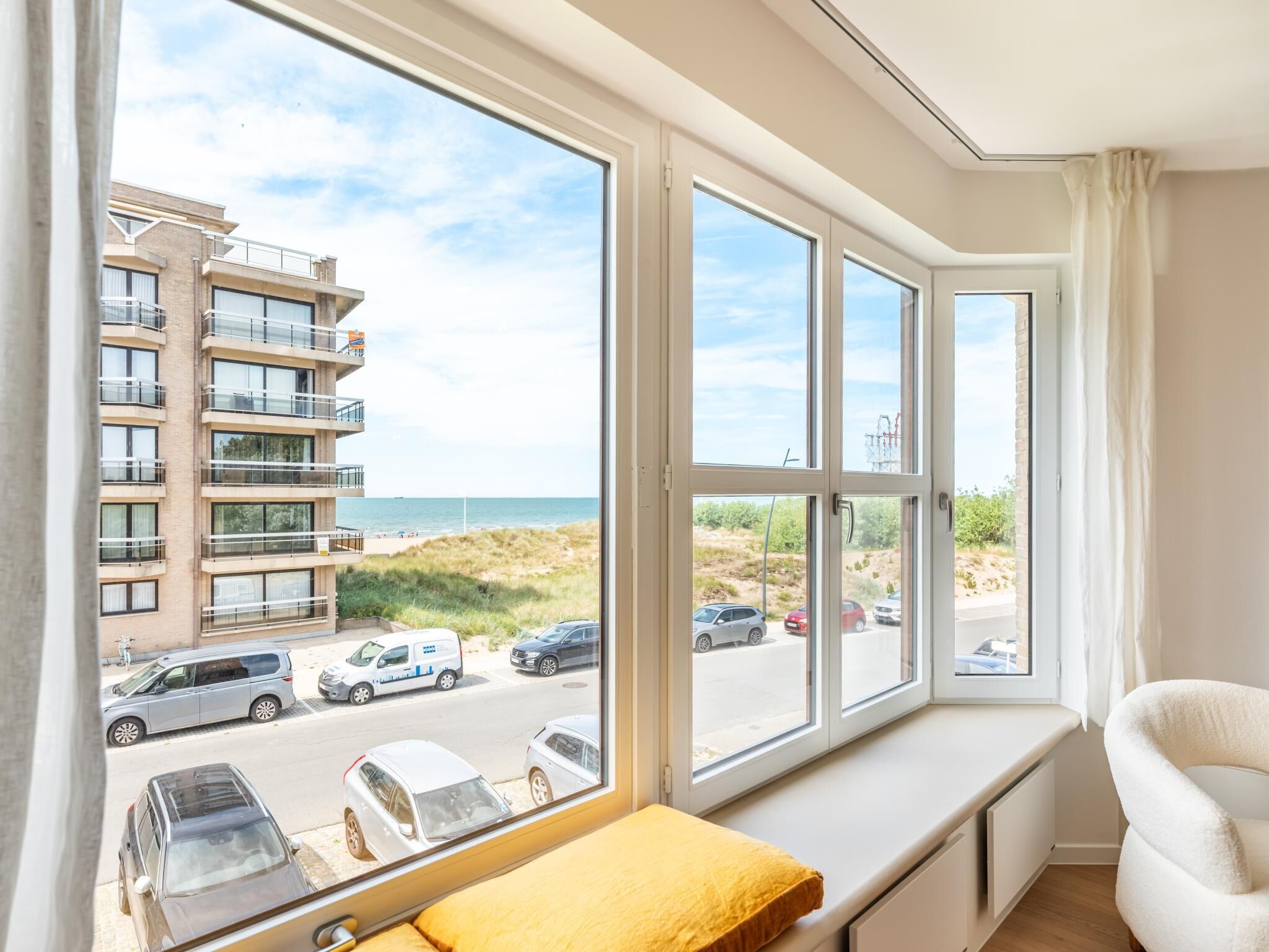 Une chambre dotée de grandes fenêtres donnant sur une plage et un parking.