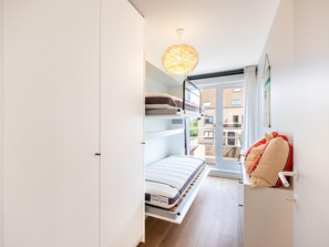 A compact bedroom with a bunk bed, a single bed, a hanging light fixture, and a view of the outside balcony. - Stylish apartment with dune view near Idesbald (Sint-Idesbald)