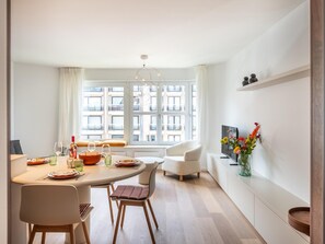 A modern dining area with a round table, chairs, and a view of the city through large windows. - Stylish apartment with dune view near Idesbald (Sint-Idesbald)
