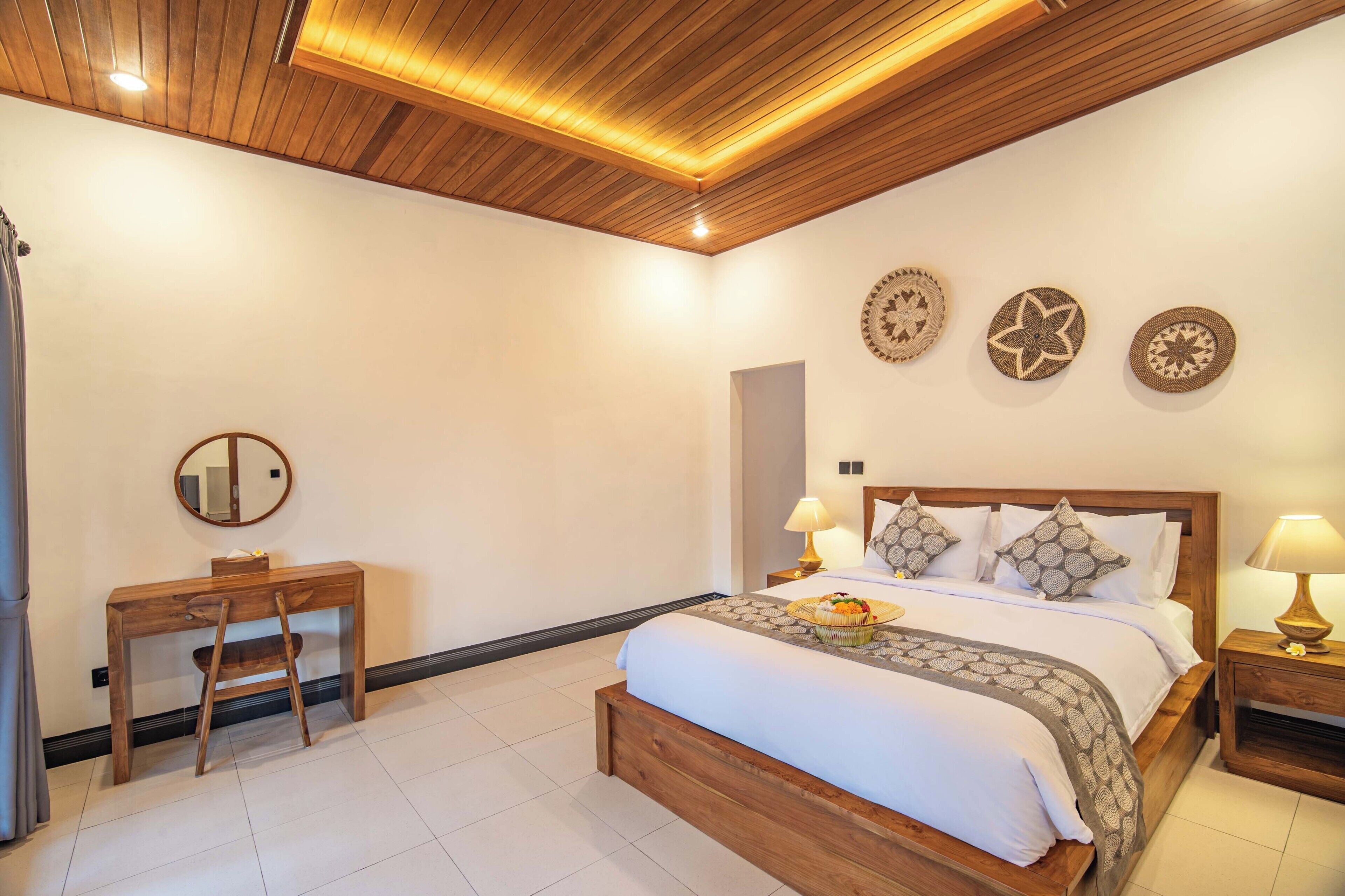 A hotel room with a wooden ceiling, a bed with patterned bedding, a desk with a chair, and decorative wall art.