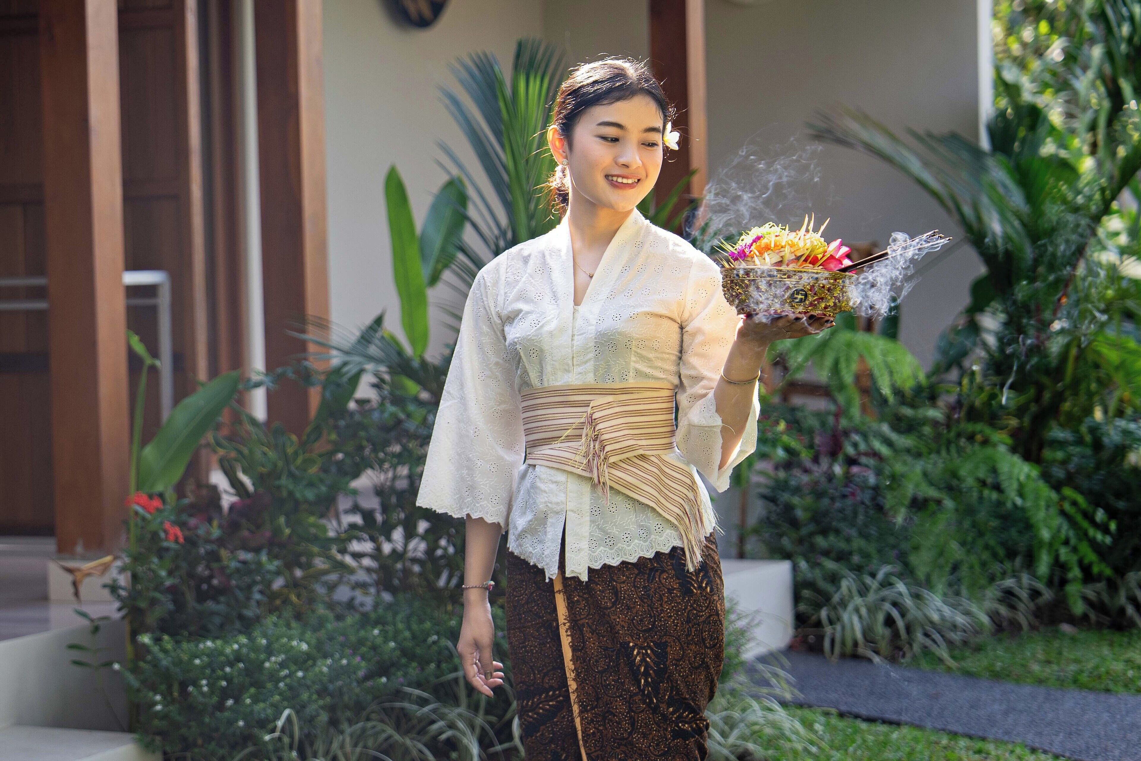 A person holding a ceremonial object outdoors with greenery in the background.