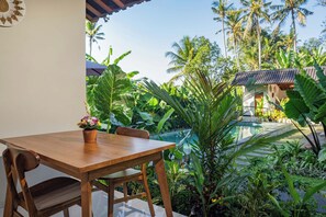 Una mesa de madera con una planta en maceta, rodeada de exuberante vegetación tropical y vistas a una piscina.
