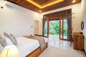 Un dormitorio con cama, mesita de noche, lámpara, cabecero de madera, ventana con cortinas y vista a la vegetación.