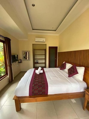 Een hotelkamer met een groot bed, een houten hoofdbord, een televisie en een raam met gordijnen.