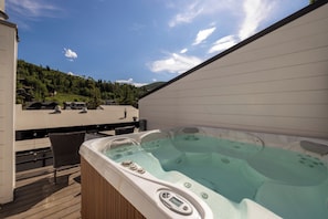 Un jacuzzi en una terraza de madera con vista a un estacionamiento y una ladera.