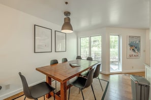 Un comedor con una mesa de madera, sillas negras y una lámpara colgante. Hay cuadros en la pared y un cartel a la derecha.