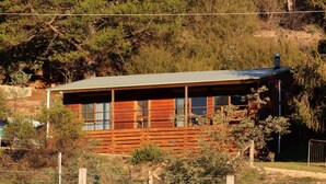 A wooden cabin with a sloped roof, surrounded by a fenced area and dense trees. - Howqua Hideaway - cozy cabin with fireplace (Howqua)