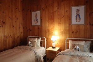 Une chambre avec deux lits, une table de chevet avec une lampe et deux tableaux encadrés au mur.