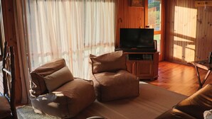 A cozy living room with a sofa, a television on a wooden stand, and a window with curtains. - Howqua Hideaway - cozy cabin with fireplace (Howqua)