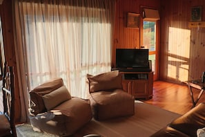 A cozy living room with a sofa, a television on a wooden stand, and a window with curtains.