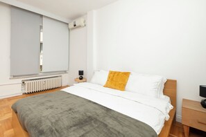 A modern bedroom with a large bed, a radiator, a window with blinds, and a bedside table with a lamp. - Bosphorus Panorama – Luxury 5BR Apartment with Balcony & AC (İstanbul)