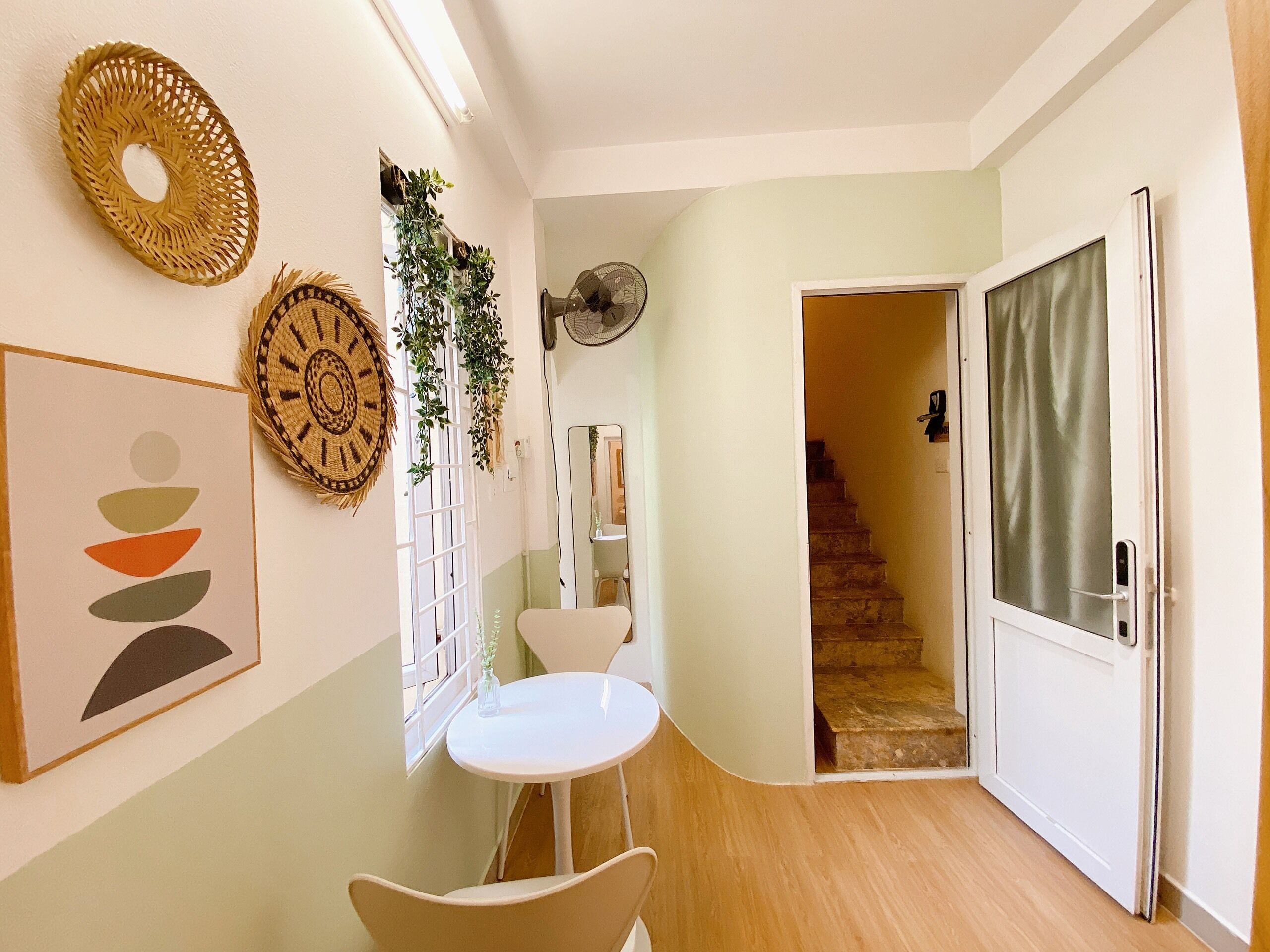 Un pasillo con una mesa y sillas blancas, un ventilador y una escalera que conduce a otra habitación.