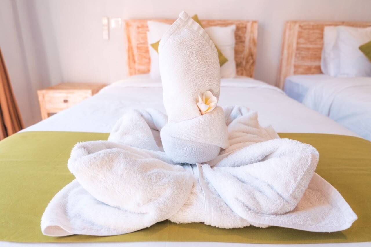 A neatly made bed with a towel arranged in a decorative manner, a green bedspread, and a wooden headboard.
