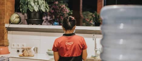 A person in a red and black uniform working at a kitchen counter with a sink and a potted plant in the background.