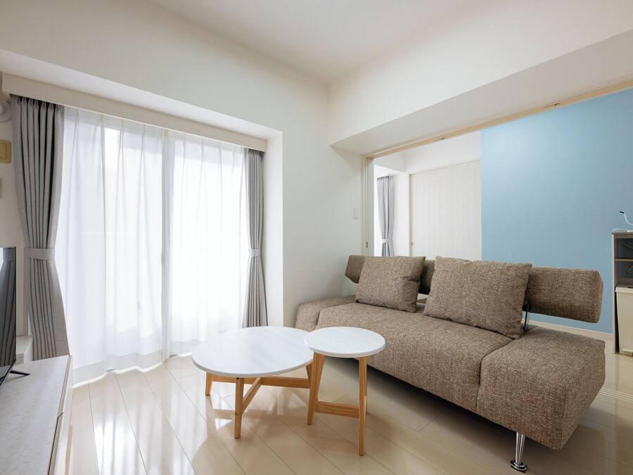 A modern living room with a sofa, two small tables, a TV, and a kitchen area.