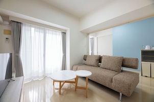 Una sala de estar moderna con un sofá, dos mesitas, un televisor y una zona de cocina.