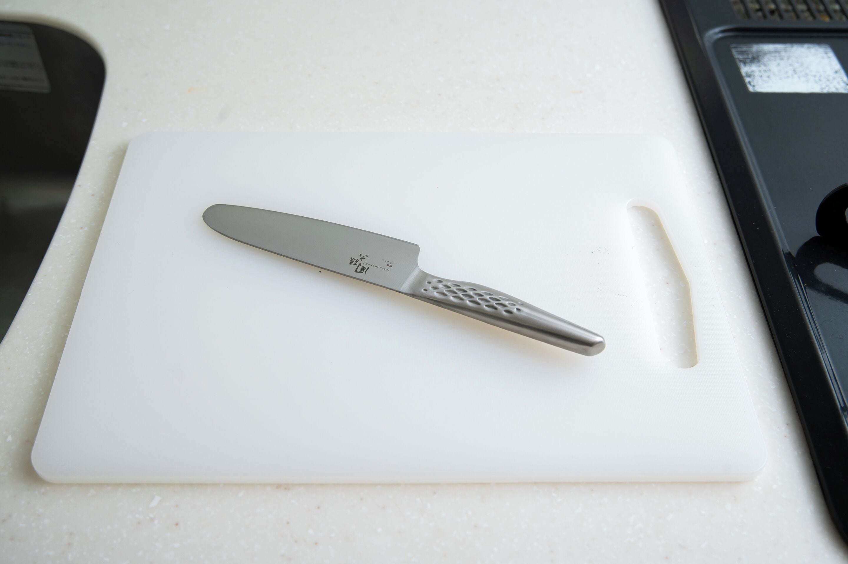 Una encimera de cocina con una tabla de cortar blanca y un cuchillo.