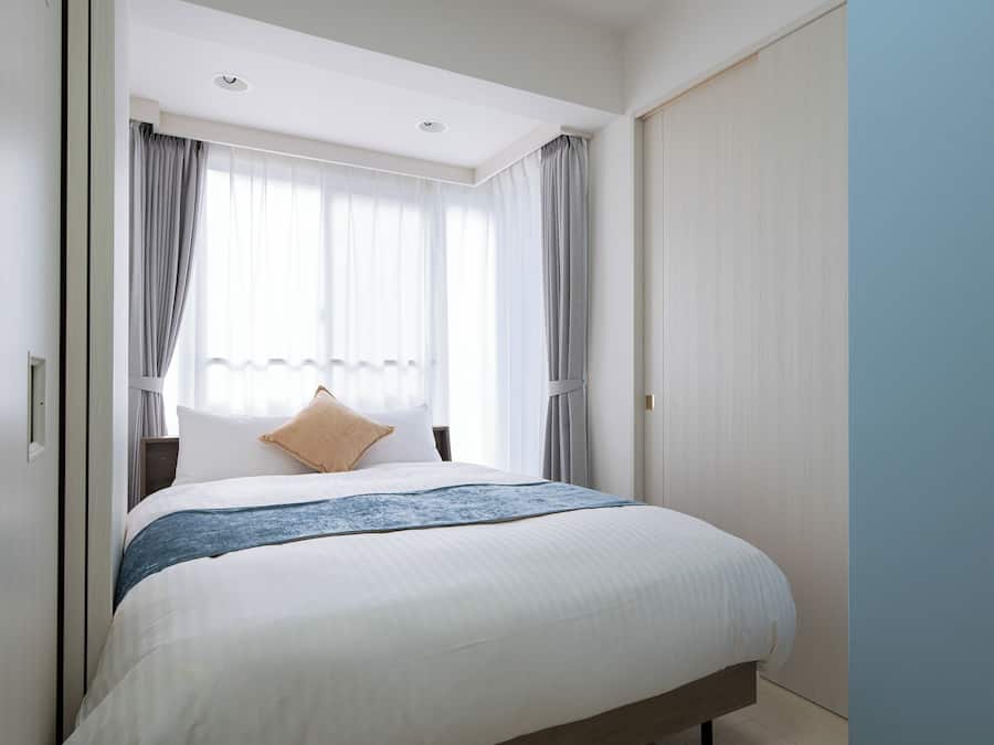 A hotel room with a bed, curtains, a window, and a door.