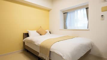 A bedroom with a bed, a window with curtains, and a wall-mounted thermostat.