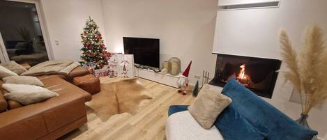 A modern living room with a fireplace, a Christmas tree, and a flat-screen TV.