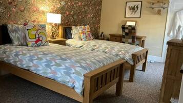 Una camera da letto con un letto grande, due comodini, una panca di legno, carta da parati floreale e un quadro appeso al muro.